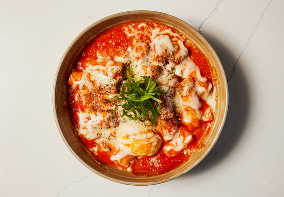 Savory Korean Tteokbokki dish with melted cheese and fresh green garnish.