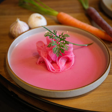 Pink pickled onions on a plate with carrots and garlic nearby.